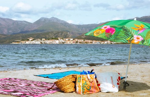 Sunshade and swimwear blurred on the beach or Plage de la Roya, in the back Saint-Florent on the