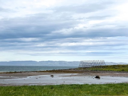 Coast with green shore, wooden racks for drying stockfish and cloudy sky over the sea, Nesseby,