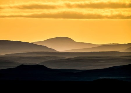 Silhouettes of mountains at sunset with yellow sky, near Vadsö, Finnmark, Norway