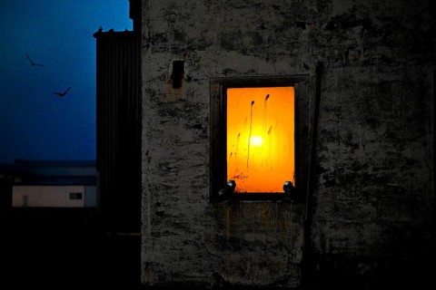 A window in a dark building through which an orange sunset shines, Vardø, Finnmark, Norway
