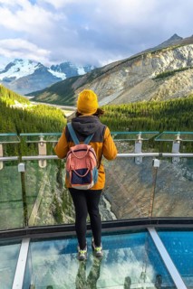 Female hiker standing on the glass platform of the glacier skywalk, contemplating the stunning