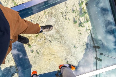 Tourists are enjoying a unique perspective, walking on a glass floor high above a rocky mountain