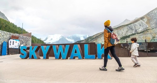 Tourists walking by large skywalk sign with athabasca glacier and mountains in background at