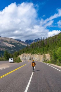 Hiker walking on the icefields parkway in the canadian rockies with a camper van parked on the side