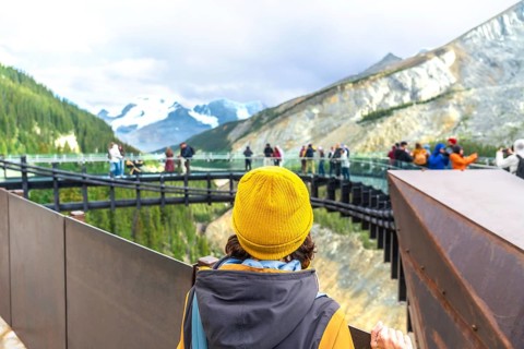 Tourist wearing a yellow beanie stands on a viewing platform, admiring the stunning view of