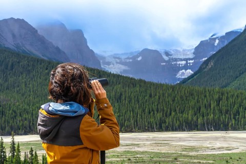 Tourist wearing an orange jacket uses binoculars to observe a glacier in the canadian rockies,