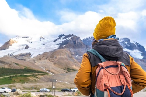 Hiker wearing a yellow beanie and carrying a backpack enjoying the breathtaking view of the