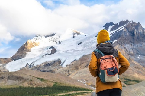 Female tourist wearing a yellow woolen hat and carrying a backpack is contemplating athabasca