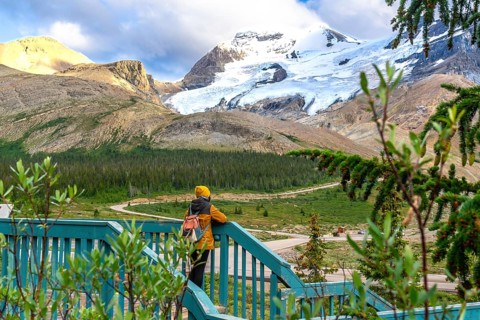 Tourist wearing a yellow beanie and jacket, leaning against a wooden fence, admiring the