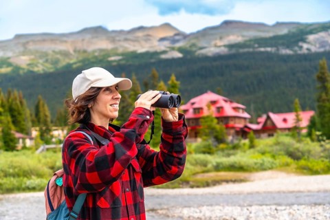 Female tourist using binoculars enjoying the landscape at bow lake with the iconic num ti jah lodge