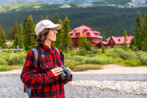 Female tourist holding binoculars enjoying the landscape of bow lake with the red roof of num ti