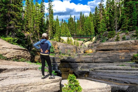 Female hiker standing on a rock formation admiring the layered rock formations of mistaya canyon