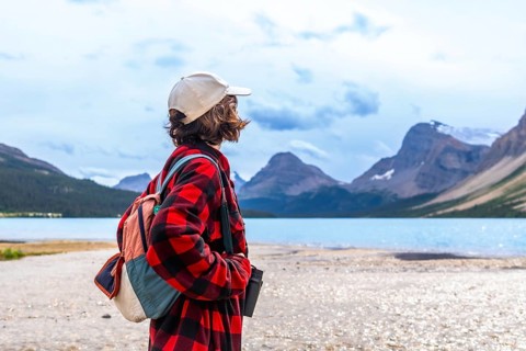 Young hiker standing on the shore of turquoise bow lake, contemplating the majestic mountains of