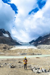 Female tourist wearing yellow jacket and backpack admiring the stunning view of the athabasca