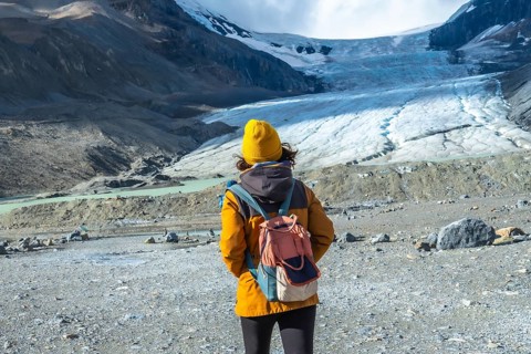 Female hiker in a yellow jacket and backpack admiring the majestic athabasca glacier in jasper
