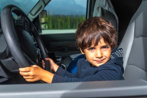 Young child playing driver while holding the steering wheel inside a car, enjoying a road trip on