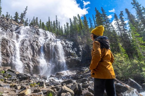 Female hiker wearing yellow beanie and jacket is admiring cascading waters of tangle creek falls in