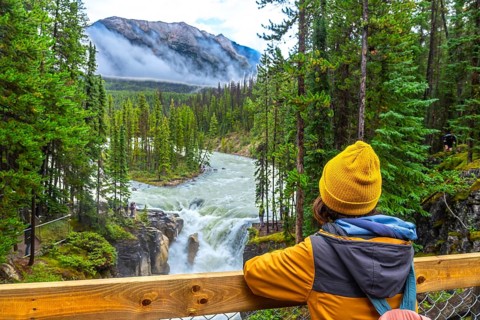 Young hiker wearing a yellow beanie and jacket admiring the stunning view of sunwapta falls in