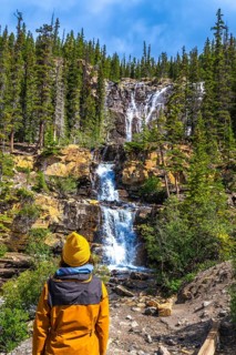Hiker in a yellow jacket and beanie contemplating the cascading waters of tangle creek falls in