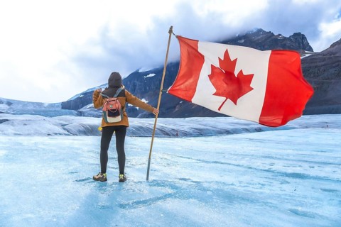 Female tourist is holding large canadian flag while standing on surface of athabasca glacier in