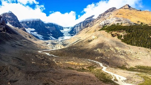 Sun shining on athabasca glacier in the canadian rockies with clouds and blue sky reflecting on