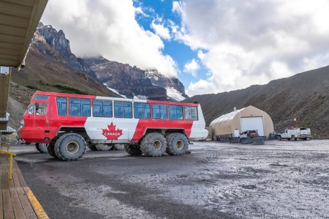 Large all terrain bus with a canadian flag parked near athabasca glacier in columbia icefield,