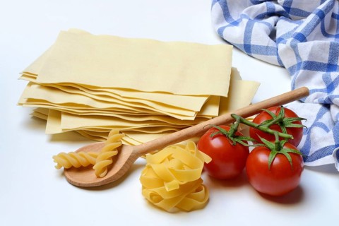 Lasagna, dried lasagna leaves, fusilli and fettuccine noodles with tomatoes and cooking spoon