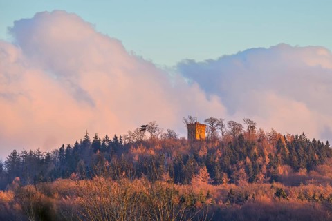 Hill with the tower of Diedrichsburg, surrounded by forests, under a pastel-colored sky in the