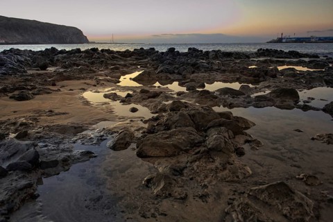 Rocks and puddles on the beach at sunrise, calm sea in the background, Los Cristianos Tenerife