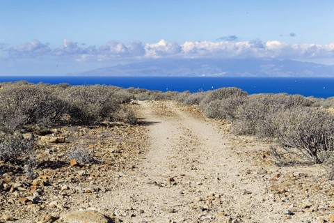A hiking trail leads through the barren landscape with views of the distant sea, Los Cristianos