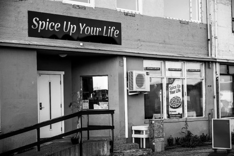 Exterior view of a restaurant with the sign 'Spice Up Your Life' in black and white, daisies