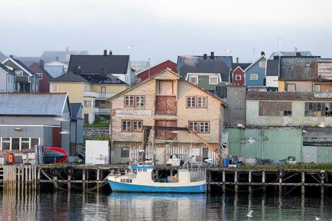 A fishing boat is lying in front of old wooden houses in a quiet harbor, surrounded by morning