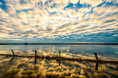 Sky with dramatic clouds is reflected in calm water at sunset, creating a peaceful and impressive
