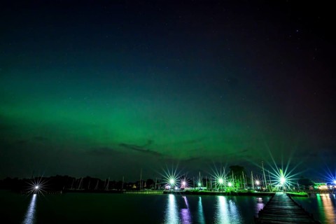 Glowing polar lights in shades of purple and green in front of an illuminated harbor on Lake