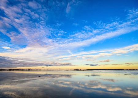 Extensive landscape with blue skies and clouds reflected in the water, soft yellow light on the