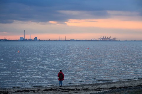 Person on the beach with a view of the sea and industrial areas in Wilhelmshafen right Jade-Weser