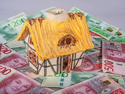 Small decorative ornamental cottage standing on Swedish 500 and 200 kronor banknotes. Symbol image