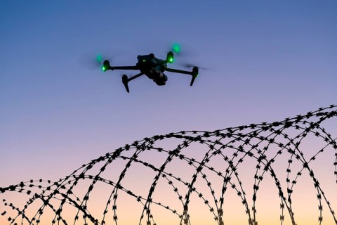 Symbolic picture, illuminated drone flying over barbed wire against the evening sky, airport,
