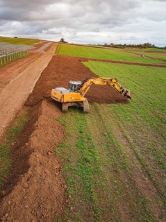 Excavator moves soil over a wide field under cloudy sky, Energiewende, construction of PV open