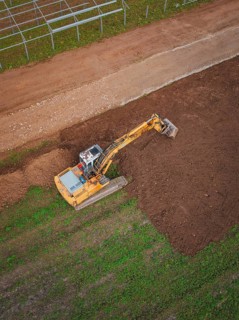 Excavator shapes the earth on a large field viewed from above, Energiewende, construction of PV