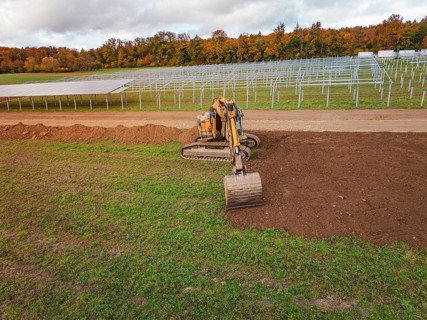Excavator working near solar panel structures with autumn leaves in the background, energy