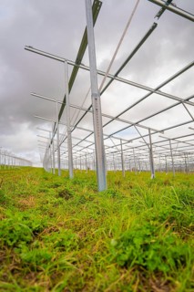 Close-up of metallic solar frames in the construction phase on a green field under cloudy sky,