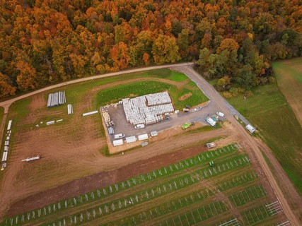 Large-scale warehouse with building materials and vehicles, surrounded by autumn landscape and