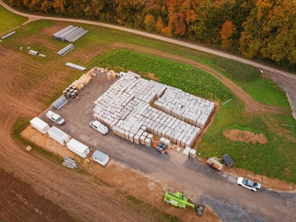 Warehouse with building materials and vehicles, surrounded by fields and an asphalted road, energy