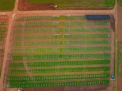 Large-scale solar frame construction on a field, surrounded by farmland seen from the air, energy