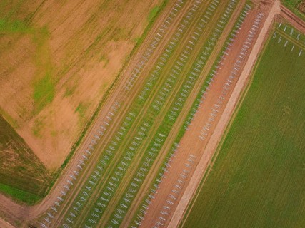 Aerial view of fields with staggered solar frame placement, surrounded by brown and green areas,