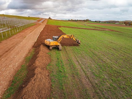 Yellow excavator shovels soil and redesigns the field, energy transition, construction of PV open