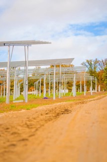 Unpaved road leads past metal structures for solar panels under blue sky, Energiewende,