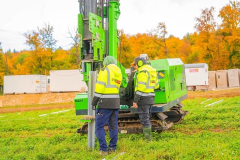 Two workers work with a green machine in front of autumn trees in a meadow, Energiewende,