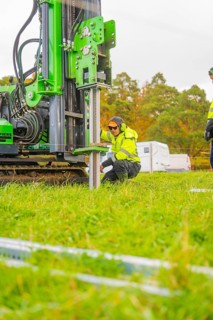 A worker kneels next to a drilling rig in a meadow and adjusts the machine, Energiewende,